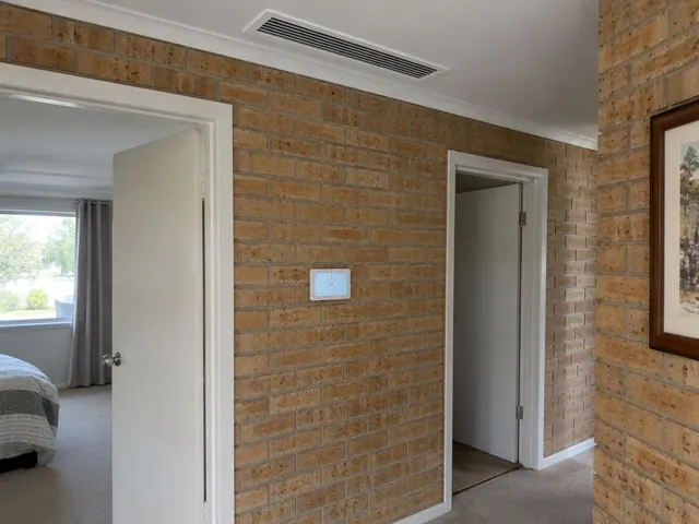 Hallway with a ceiling duct outlet and wall controller on a brick wall in Greenwith