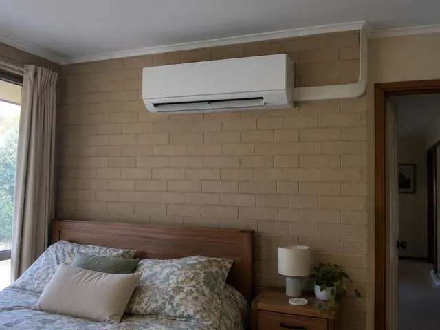 Wall-mounted split system on a brick bedroom wall above a bed in Golden Grove
